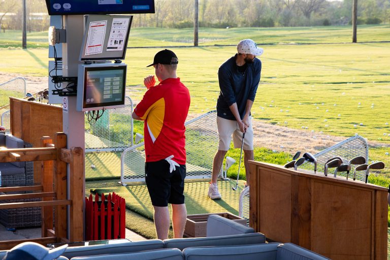 Two males hitting golf balls on the driving range during a TopCityGolf league event